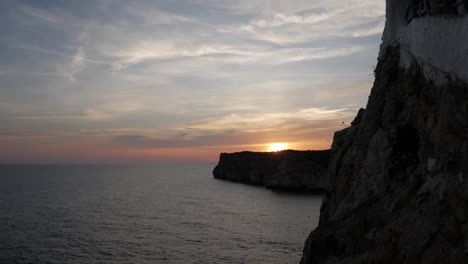 sunset over rocky cliffs with calm ocean water at cova d'en xoroi, mallorca
