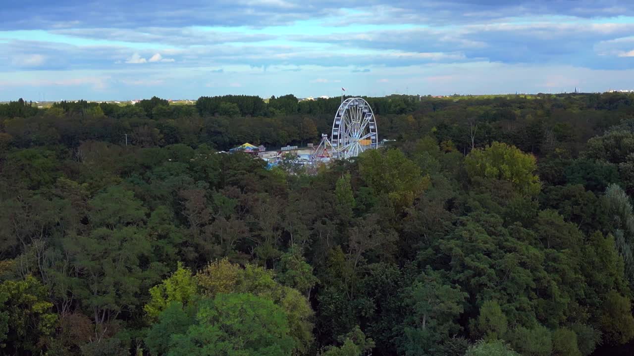 outdoor forest fairground, funfair, carnival with rides and stalls surrounded by forest. Smooth aerial view flight descending drone