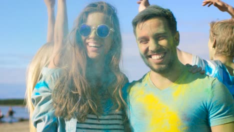 retrato de una pareja feliz cubierta de colorido polvo bailando en el festival de holi. la gente en el fondo se divierten lanzando polvo de holi