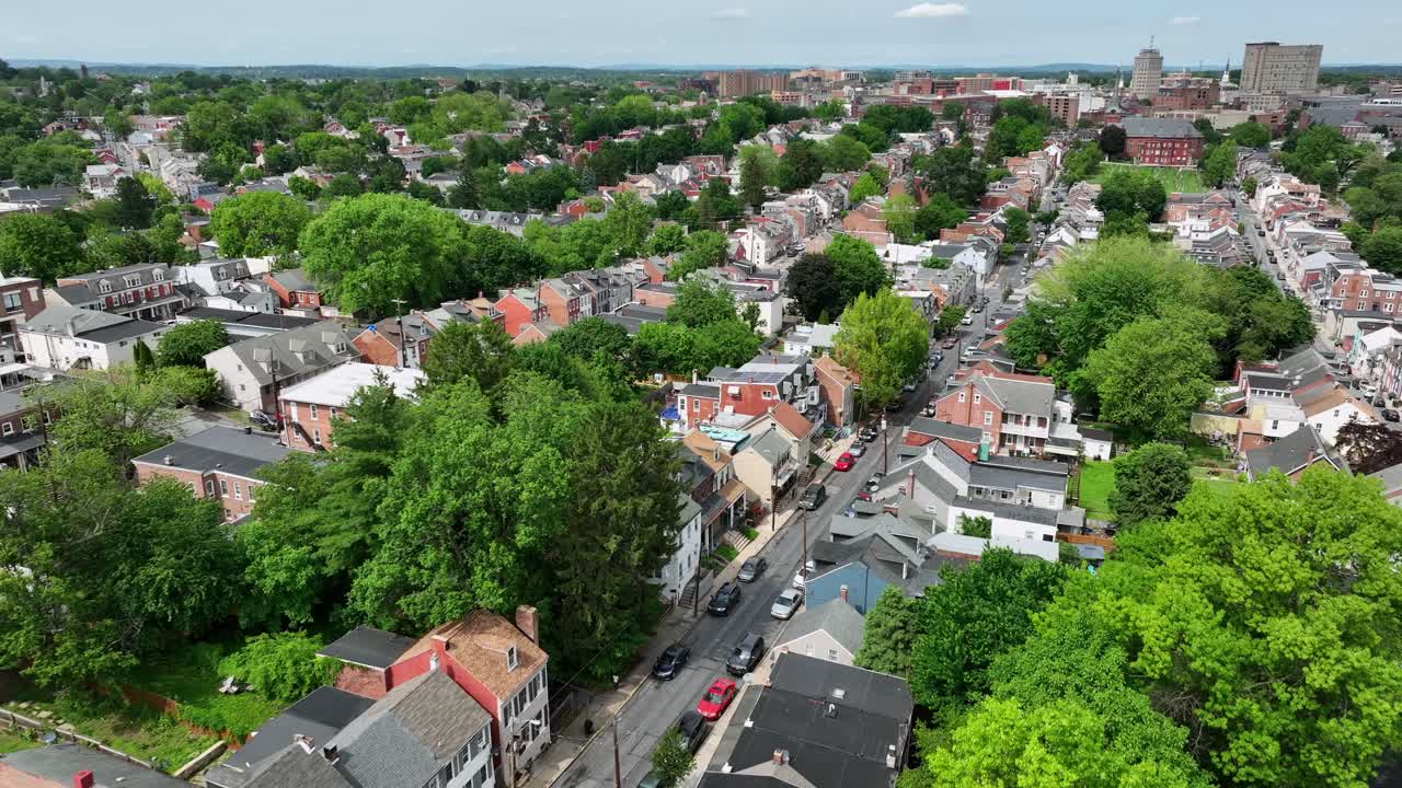 Aerial establishing shot of american town historic row of houses in different colors. Sunny day with green spring trees in May. Wide shot.Middle class housing area in suburb and downtown in background