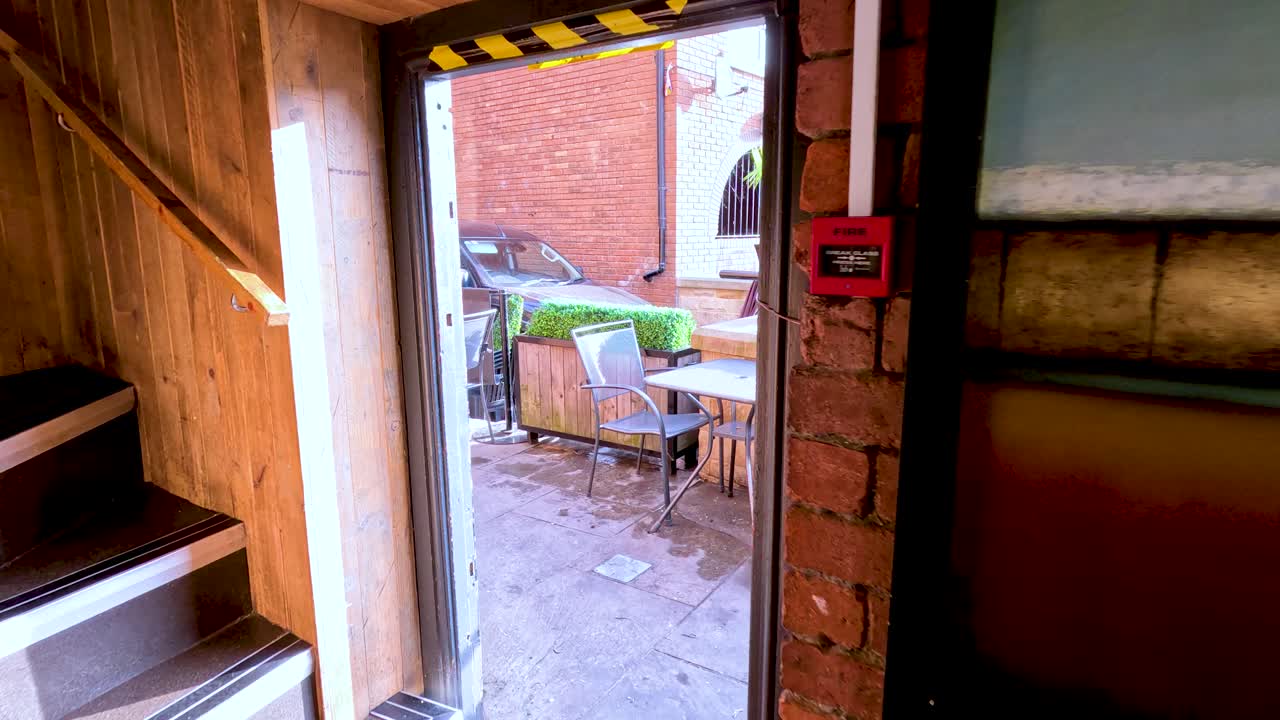 A person exits a brick café onto a riverside patio, revealing outdoor seating and a scenic urban river view under bright daylight with smooth camera movement