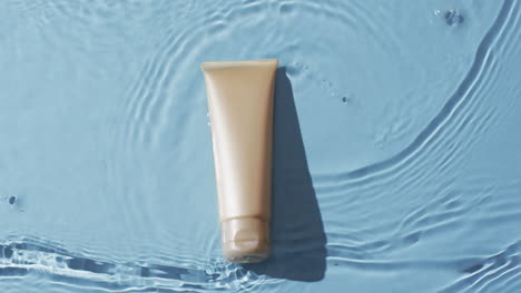 video of beauty product tube in water with copy space on blue background