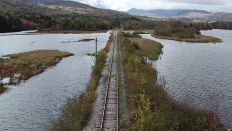 Flug-über-Eisenbahnschienen-Zwischen-Fluss-Während-Des-Herbstlichen-Berges-Im-Hintergrund