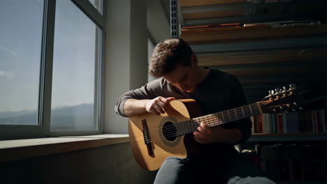 Young Man Playing Acoustic Guitar by a Window