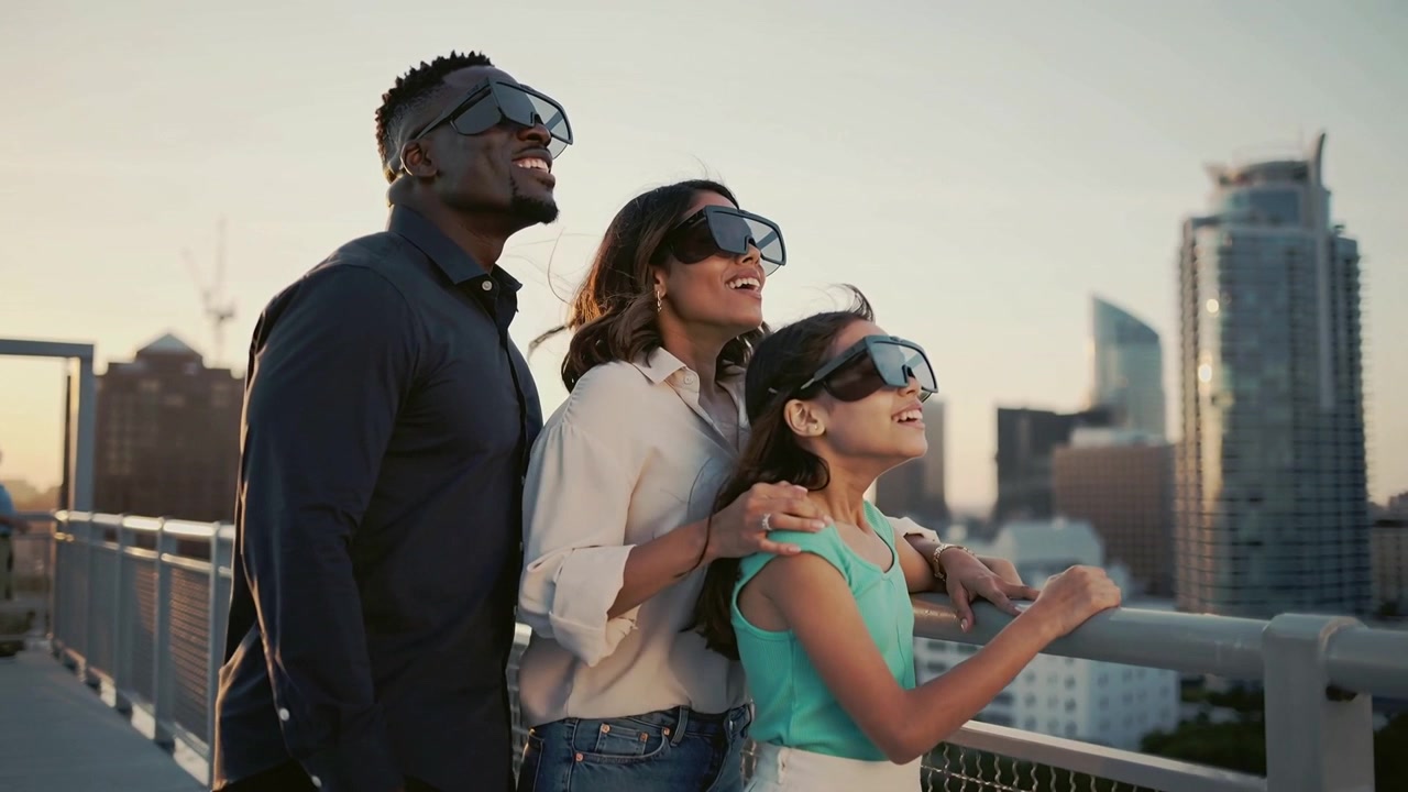 Famiglia che guarda in alto dalla ringhiera sul ponte, seguendo un'interfaccia AR sopra lo skyline, indossando visiere