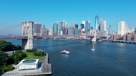 drone aerial landscape of yacht ship ferry passing under brooklyn bridge new york city cbd skyline manhattan usa america east river infrastructure buildings skyscrapers