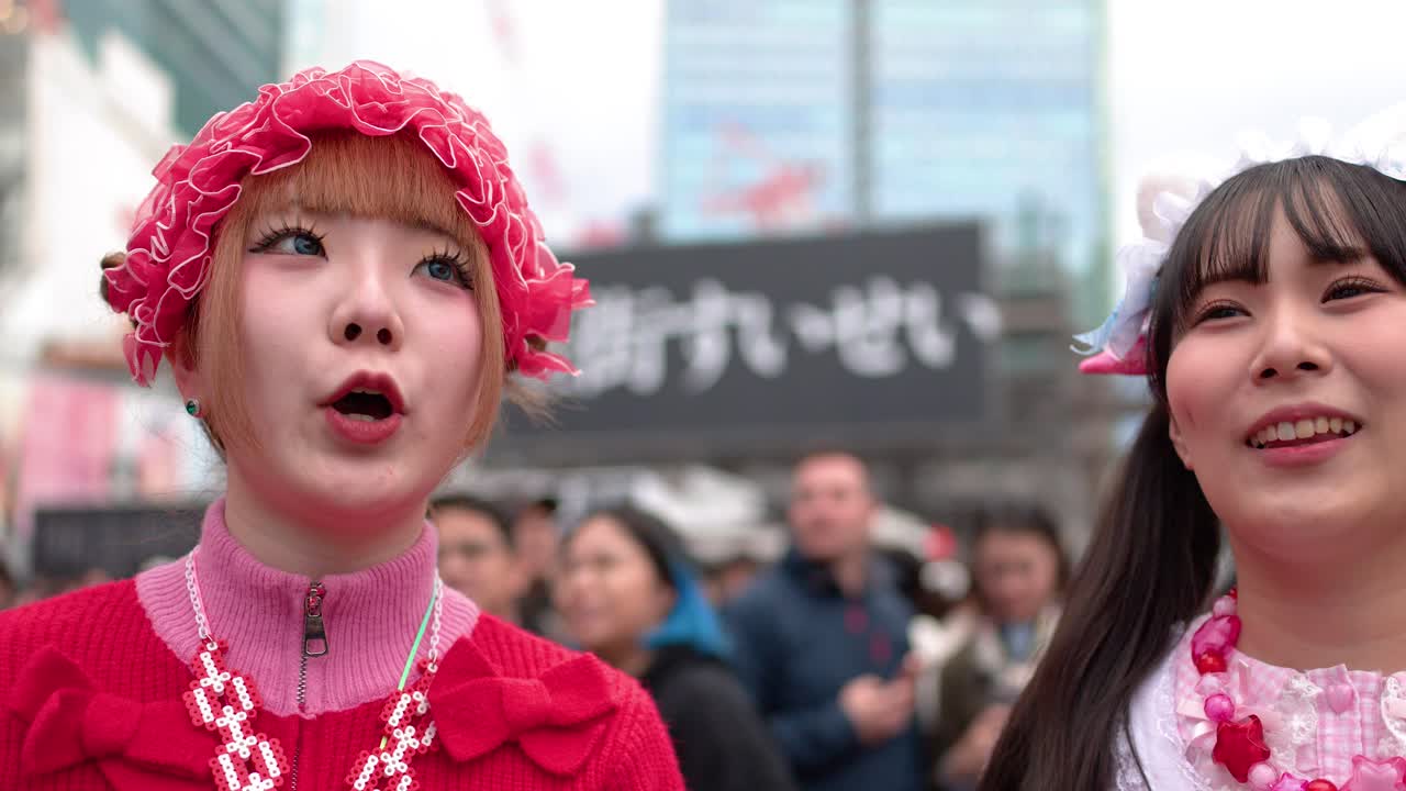 兩位年輕女士穿著色彩繽紛的原宿Decora時尚服飾，在熱鬧的東京有說有笑。