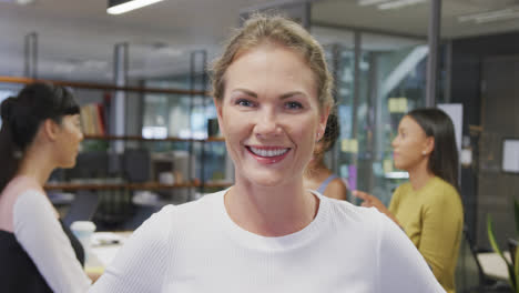 Portrait-of-happy-caucasian-businesswoman-over-diverse-business-colleagues-discussing