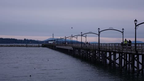 pan with people walking on a long pier leading towards a break water in ocean during the evening clouds at dusk