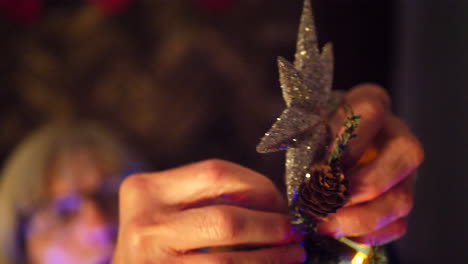 A-woman-hanging-a-sparkling-star-ornament-on-top-of-a-Christmas-tree-during-the-holiday-season