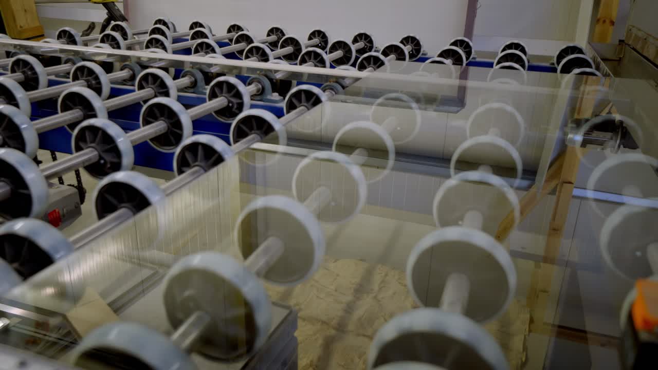 Glass sheet moving through industrial processing line with automated rollers in factory. Modern manufacturing process with precision machinery and clean production environment