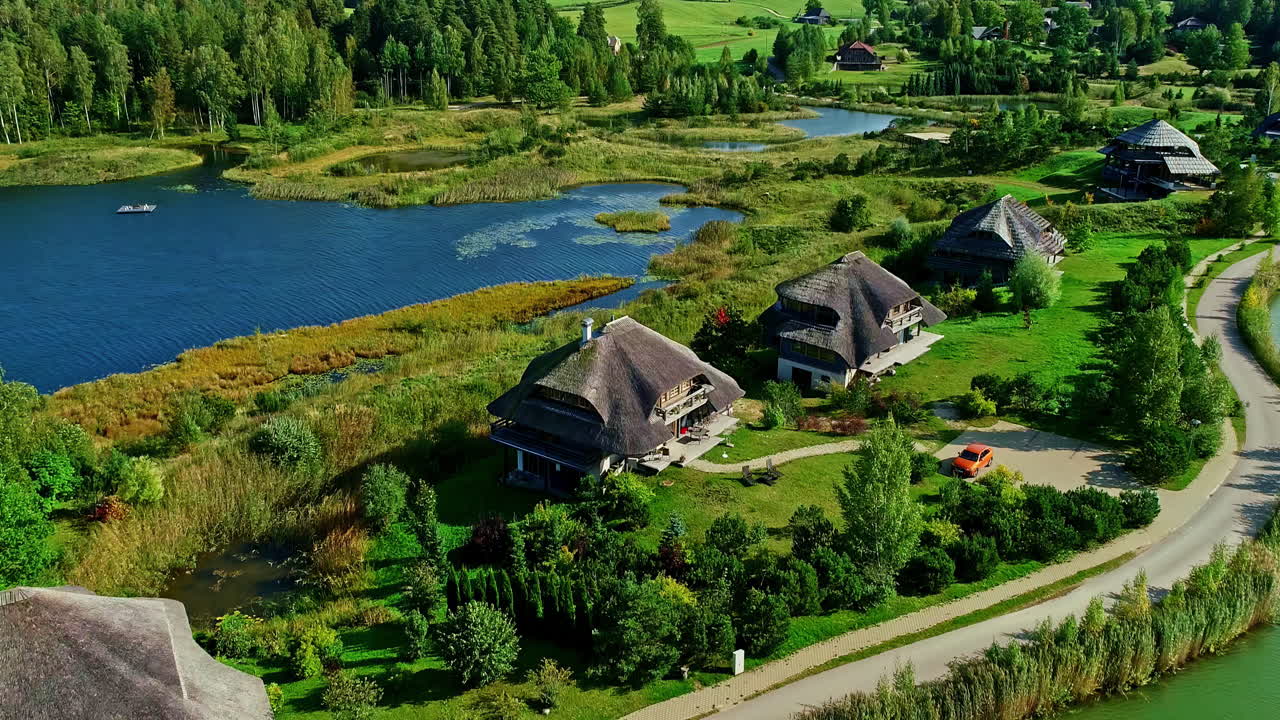 Luftfoto af traditionelle taghuse ved en sø og grøn fyrreskov i dagslys