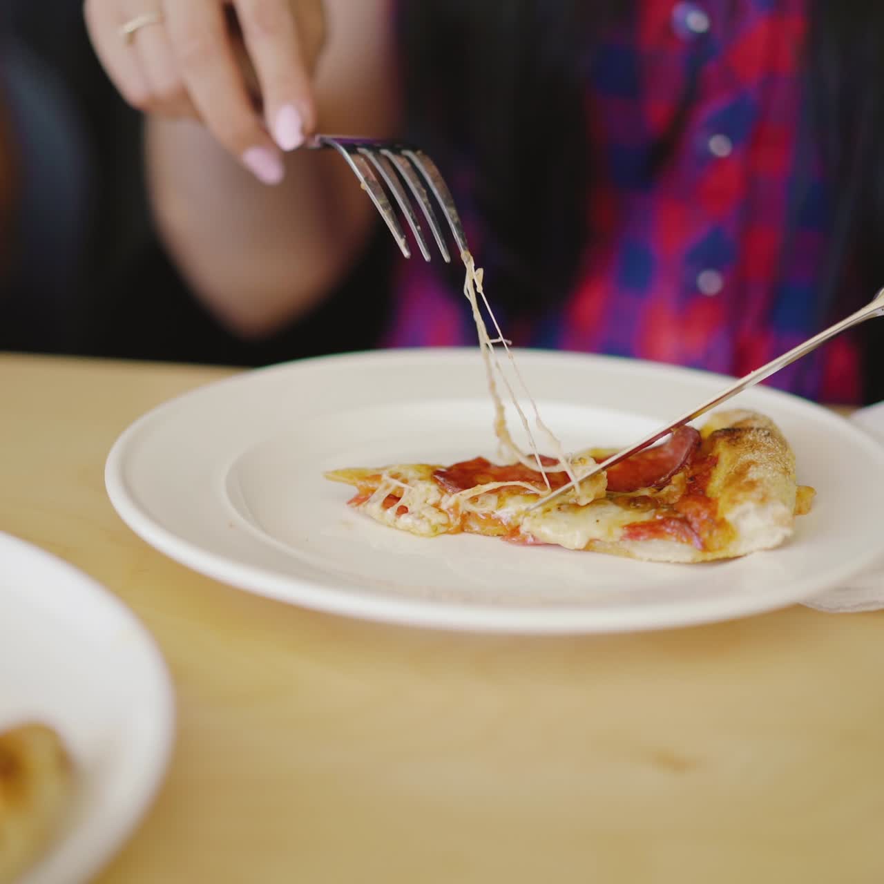 woman is cutting a piece of hot pizza and putting it in her plate at the table in the pizzeria. Blurred background