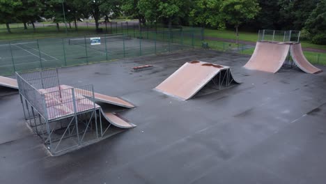 aerial view flying low descending view across fenced skate park ramp in empty closed playground