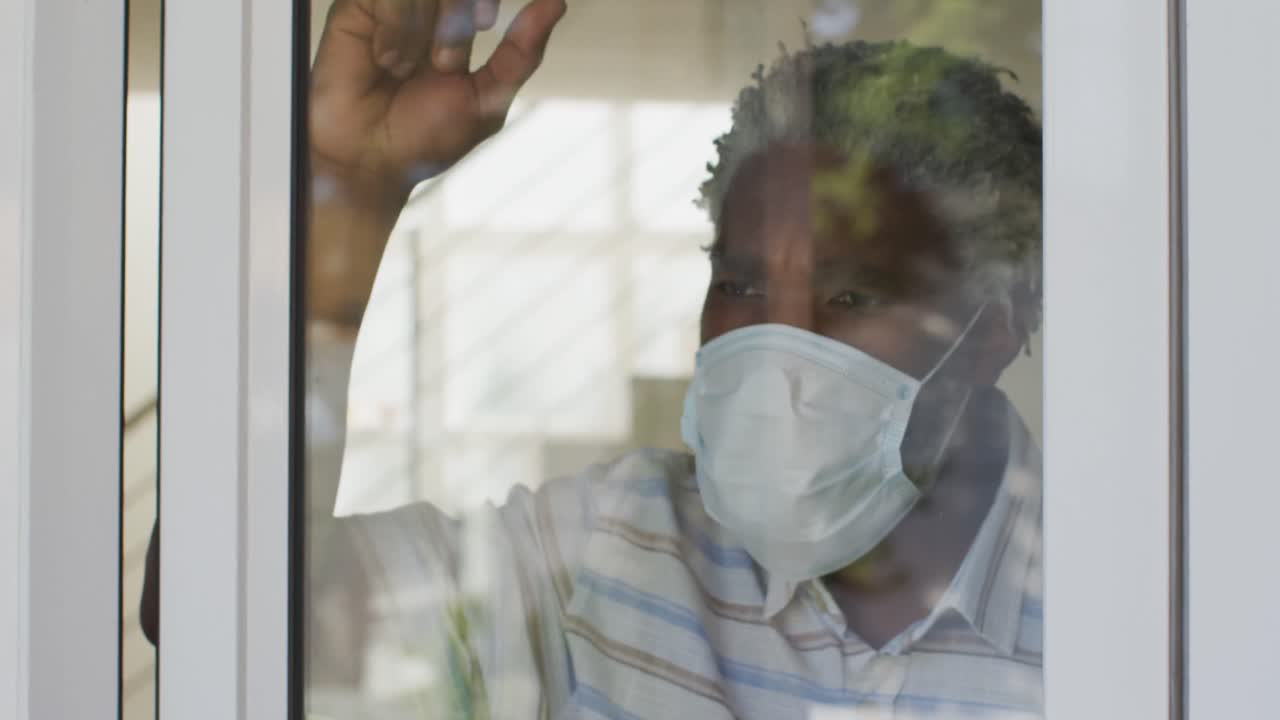 Senior man wearing face mask looking out of window at home