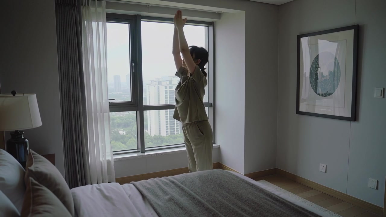 Starting stretch lady in loungewear reaching up and bending forward at window by bed toward skyline