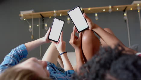 happy diverse female friends lying on bed and using smartphones with copy space at home, slow motion