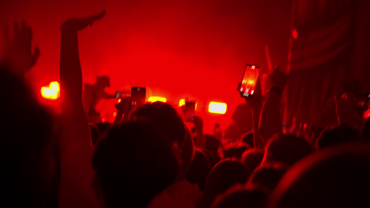 Pubblico a un concerto che registra un'esibizione dal vivo con smartphone sotto luci rosse