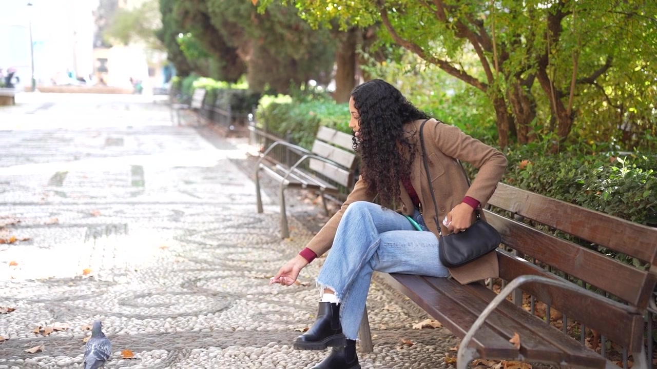 Una giovane donna cerca vari oggetti nella sua borsa mentre è seduta in un parco.