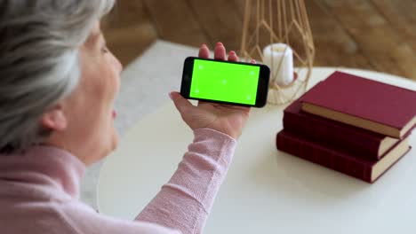 mujer madura de edad avanzada con cabello gris y una llamada de video en su teléfono inteligente. teléfono inteligente con una pantalla verde