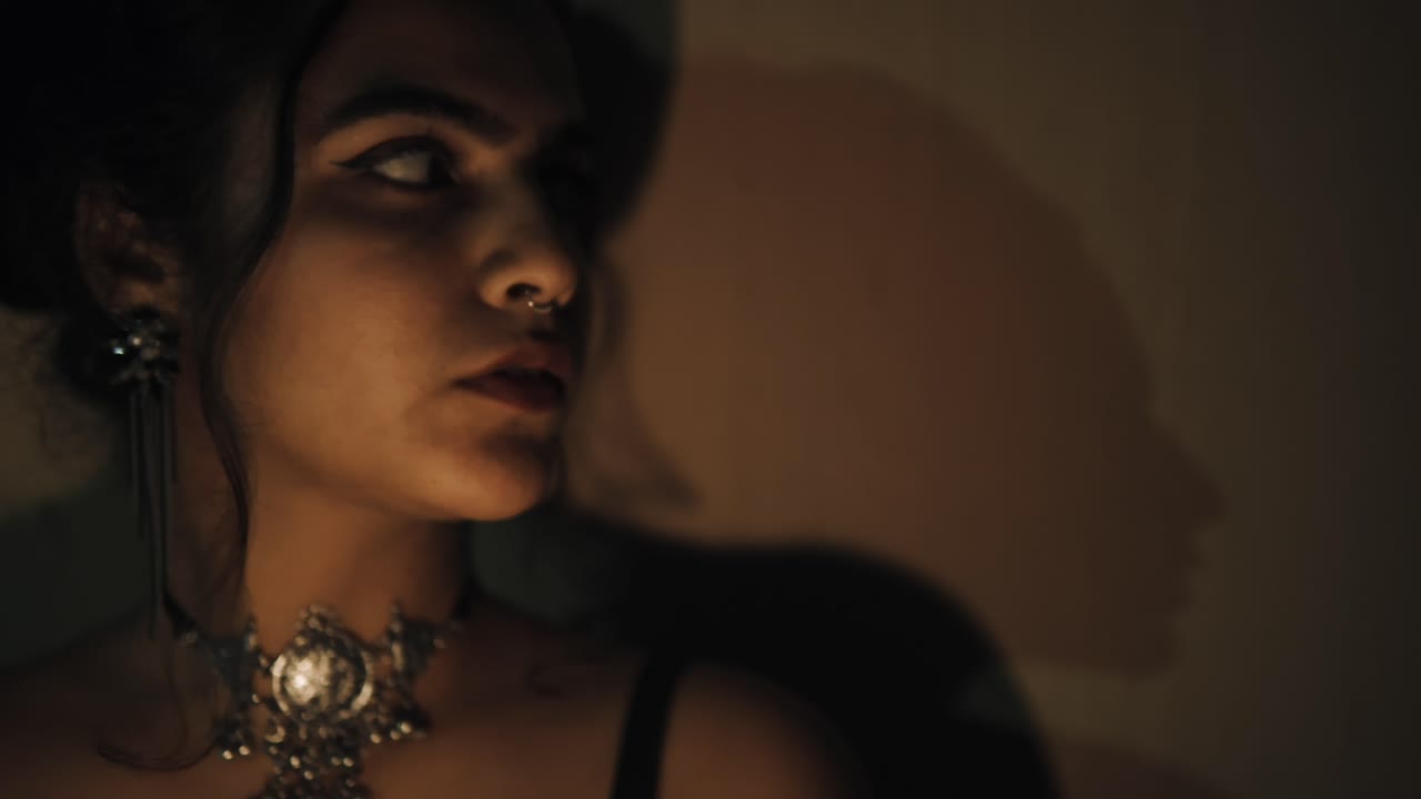 Front view of pretty woman looking to side with face lit with shadows in background in the dark