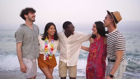 portrait of five young multicultural friends on the sea shore laughing. multiracial young women and men strolling along a beach.