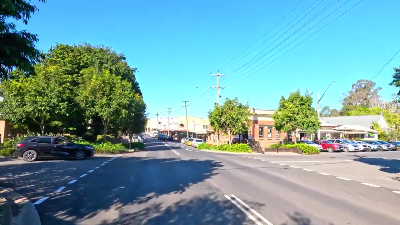 Un travelling grand-angle traverse la rue principale ensoleillée d'une petite ville australienne avec de la circulation.