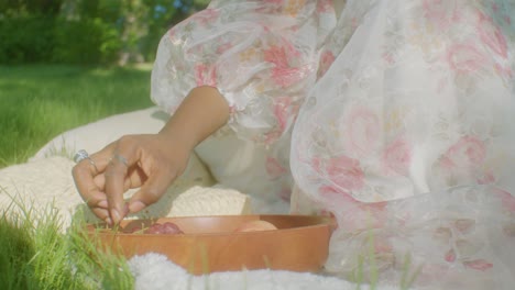 Ethiopian-woman-on-picnic-in-park-under-trees-in-shade-eats-grapes,-slomo