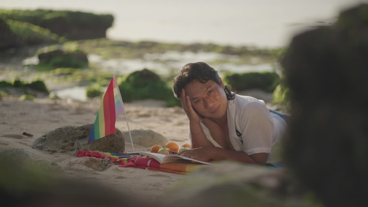 Man Reading on Beach with Pride Flag