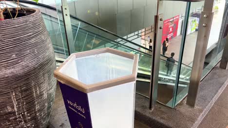 a person disposes of trash in a bin at a modern mall. bright lighting and clean environment emphasize responsible waste disposal