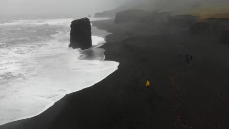 girl in yellow raincoat walking in a storm along a black beach in djupavogshreppur, iceland-1