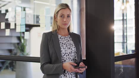 Portrait-of-caucasian-businesswoman-using-smartphone-smiling-looking-at-camera