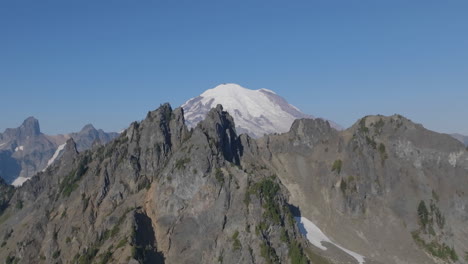 Fast-aerial-fly-through-of-rocky-ridges-and-mountains-with-Mount-Rainier-in-the-background-covered-in-snow