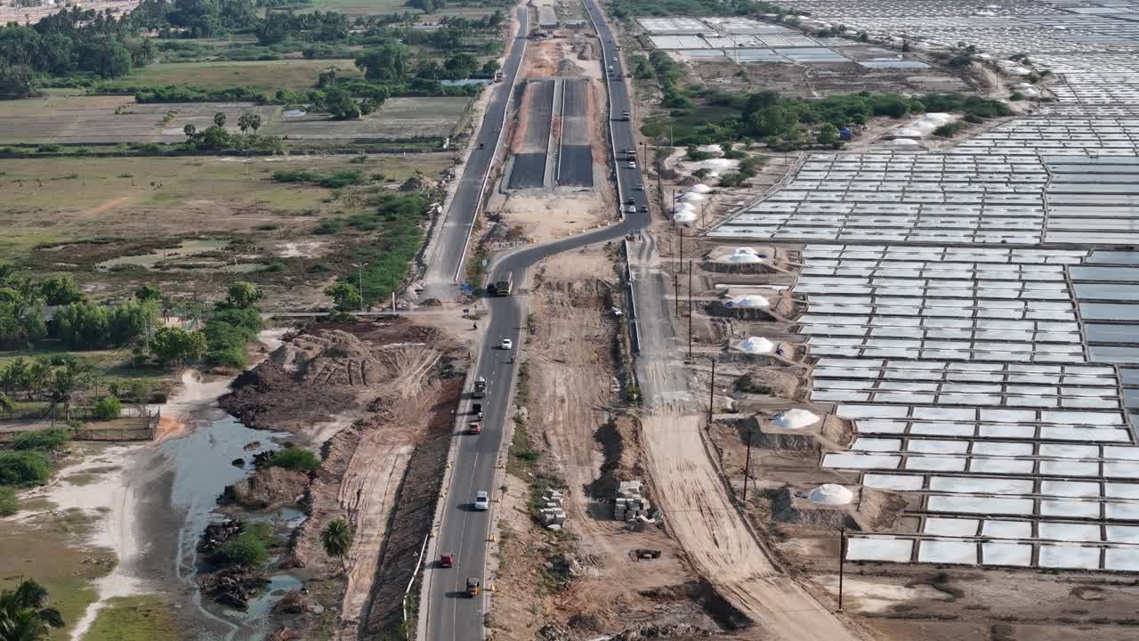 Aerial footage of a new highway's progress, cutting through an industrial zone of salt pans and natural fields, symbolizing modern infrastructure's expansion