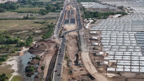 aerial footage of a new highway's progress, cutting through an industrial zone of salt pans and natural fields, symbolizing modern infrastructure's expansion