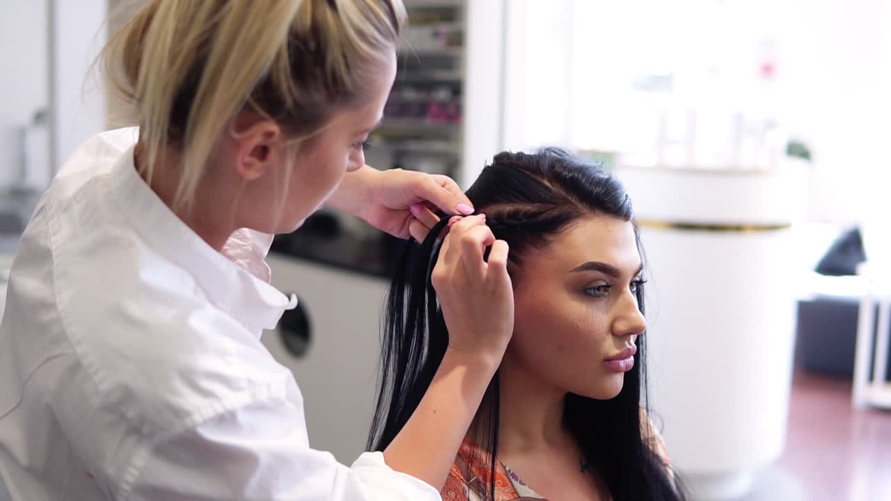 Working process of hairdresser plaiting braids to brunette girl in beauty salon. Slow motion. Close up