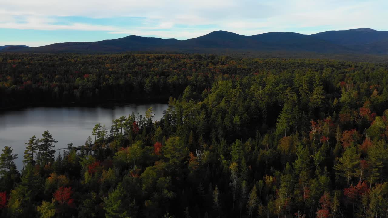 drone aéreo orbitando alrededor de un lago con coloridos árboles de otoño a lo largo de la costa cuando termina el verano y las estaciones cambian para caer en maine