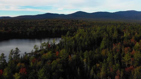 aerial drone orbiting around a lake with colorful autumn trees along the shore as summer ends and the seasons change to fall in maine