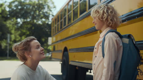 Smiling-happy-mom-chatting-with-son-at-bus.-Woman-escorting-child-to-classes.