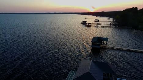 aerial view of sunset on a pristine lake as camera tilts down from suns-lashed docks into blue waters