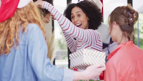 feliz mujer biracial saludando a diversos amigos en sombreros de santa con regalos de navidad en su casa
