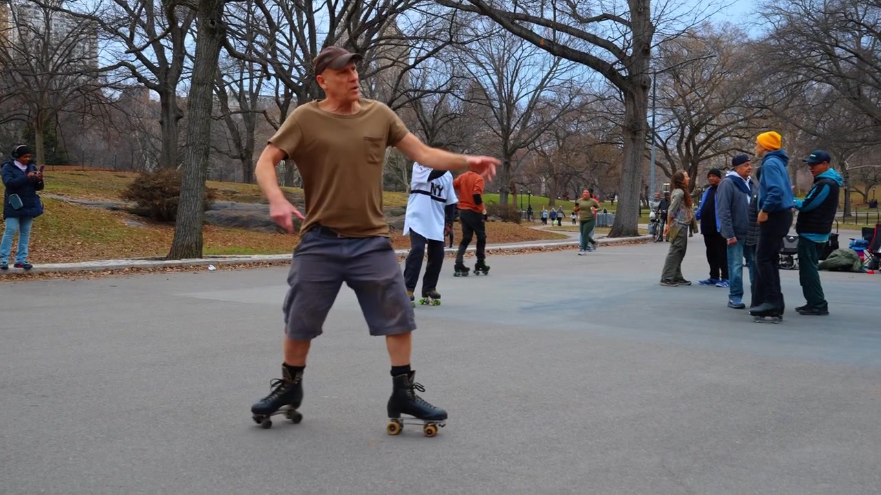 New York, USA, 8. marts 2026: Folk på rulleskøjter i Central Parks offentlige rum. Bagfra af en mand på rulleskøjter på asfalt med en gruppe mennesker, der står i en bypark