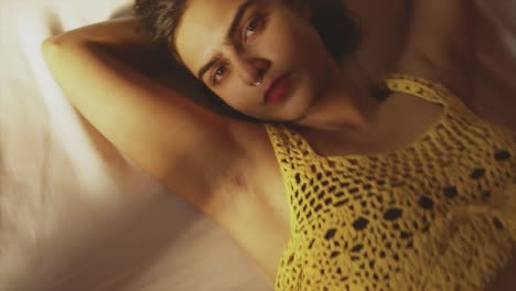 A-close-up-shot-of-the-face-of-an-attractive-Asian-female-model-in-a-yellow-tank-top,-dollying-out-to-reveal-her-beautiful-body-as-she-lies-on-a-bed