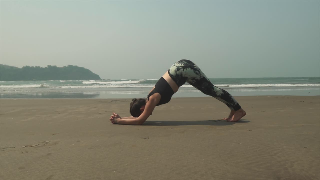 chica haciendo yoga en la playa con relajantes olas rompiendo a lo largo de la costa en segundo plano.