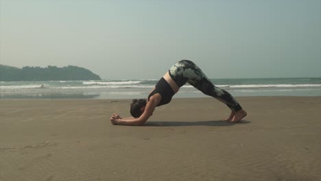 Mädchen-Macht-Yoga-Am-Strand-Mit-Beruhigenden-Wellen,-Die-Sich-Entlang-Der-Küste-Im-Hintergrund-Brechen