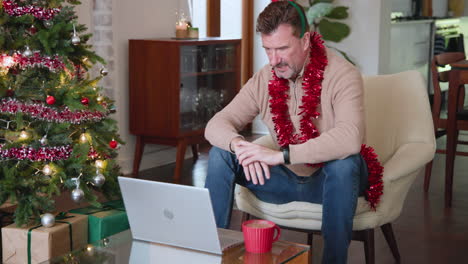 at christmas, senior man video chatting on laptop at home, wearing festive decorations