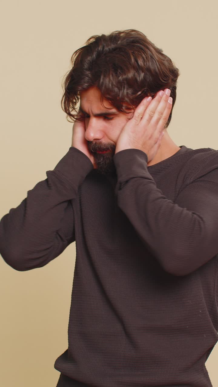 Hombre libanés frustrado, molesto e irritado cubriéndose las orejas y haciendo un gesto de negación contra un fondo beige.