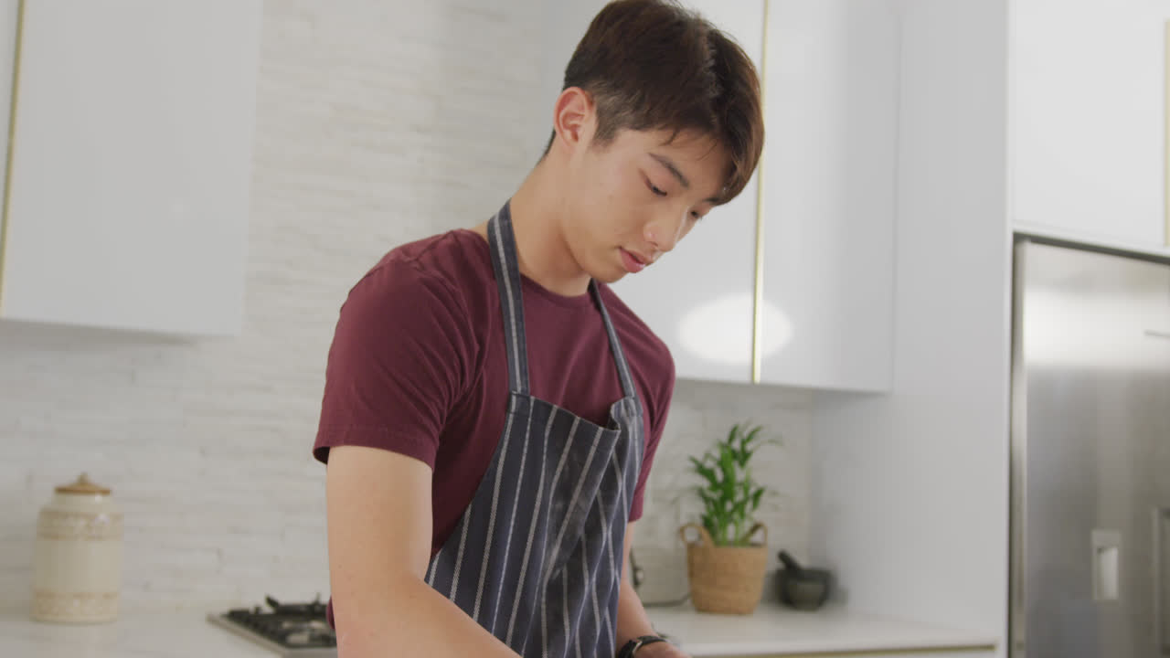 Asian male teenager preparing food and wearing apron in kitchen
