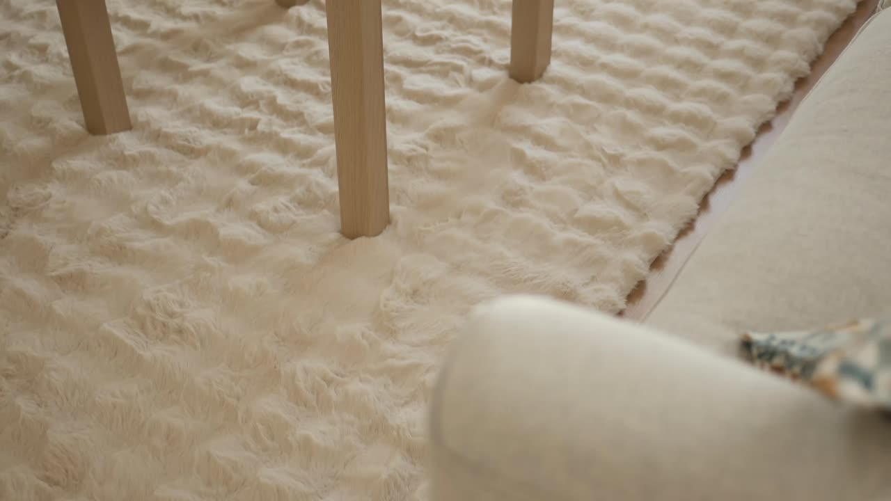 Nærbilde av mykt kremfarget fluffy teppe med bordben i tre