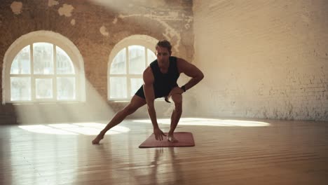 Male-gymnast-doing-fitness-in-the-solar-hall.-Sports-and-gymnastics-warm-up-for-muscle-stretching-and-strengthening.-A-guy-in-black-sportswear-goes-in-for-sports-in-a-sunny-gym